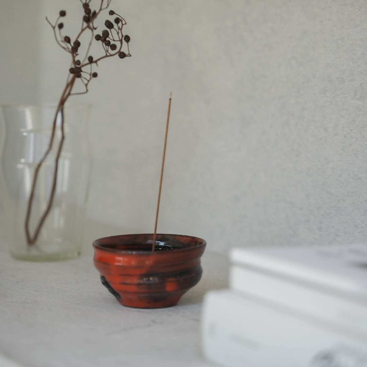 Karmosinrød japansk røgelseskar med en tændt pind på en lys hylde, der sikkert opsamler aske til en fredfyldt morgenmeditation.