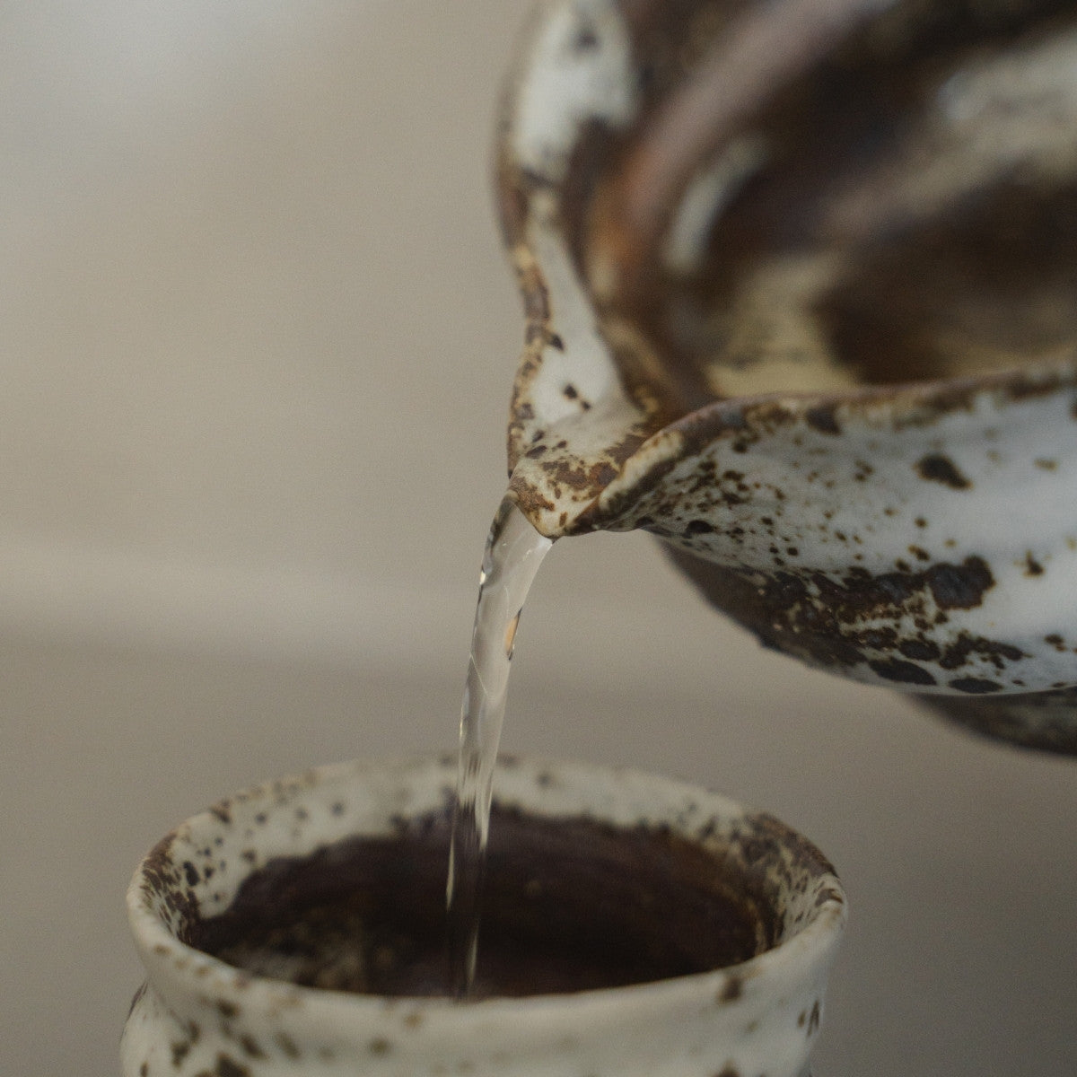 Sake pouring from a textured Zui Japanese sake carafe into a white ceramic sake cup, to effortlessly enjoy warm sake