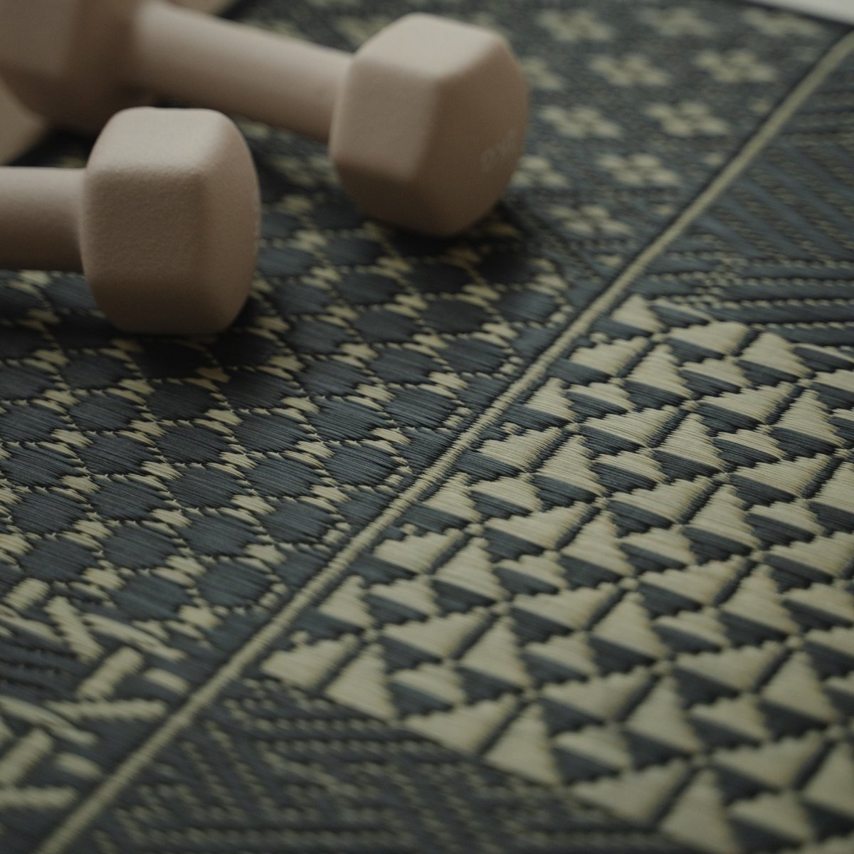 Close-up van de Japanse Tatami Yogamat "Ed Plain" Zwart met dumbbells, met nadruk op ingeweven geometrische patronen.
