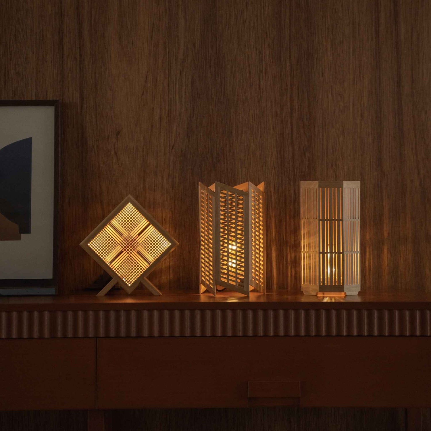 "Lit Japanese table lamp \"Kanata\", \"Towaru\", and \"Kagayaki\" glowing as ambient lamps on a mid-century modern console table."