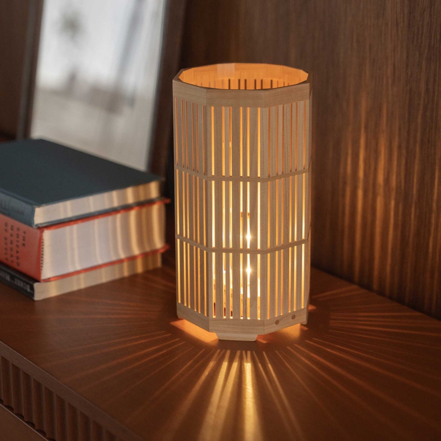 Lit Japanese wood table lamp "Kagayaki" acting as an ambient lamp, projecting radial shadows on a mid-century modern console.