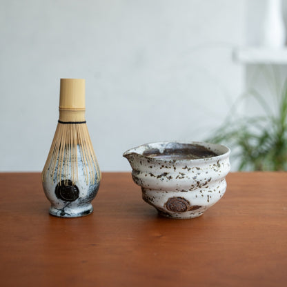 Zui uneven white spouted matcha bowl and Japanese matcha whisk stand on a wooden table for an authentic matcha ritual