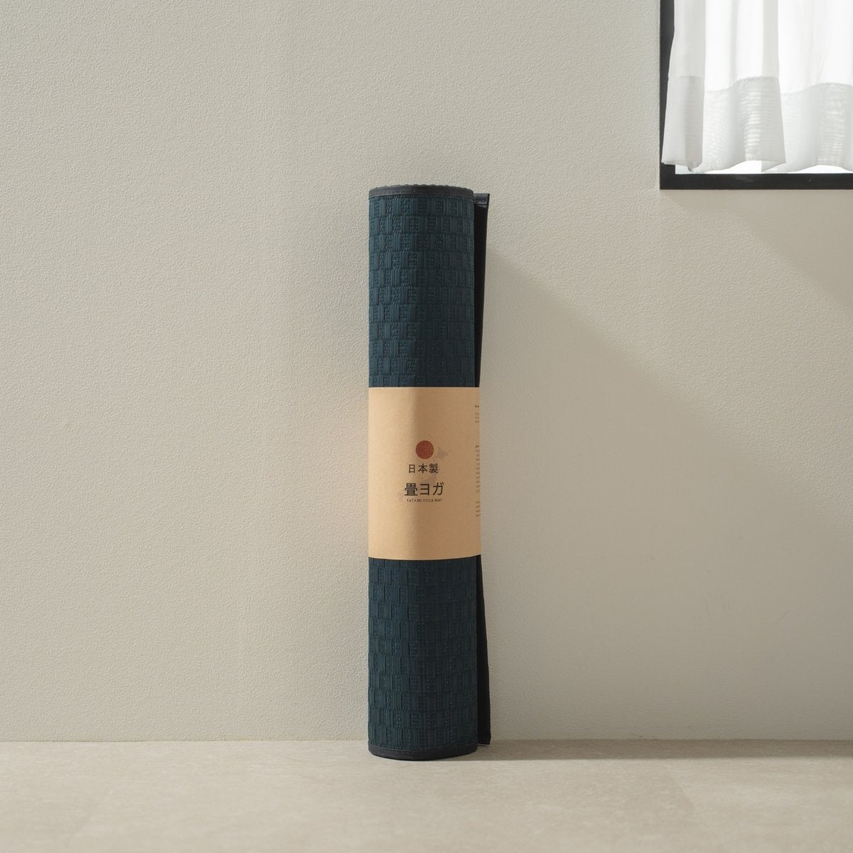 Rolled Japanse Tatami Yoga Matras "Ed Plain" Navy staand bij een helder raam, klaar voor mindfulness meditatie thuis.