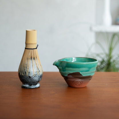 Japansk matcha-piskeris-holder og smaragdgrøn matcha-skål med tud på et træbord, klar til et dagligt morgen-te-ritual.