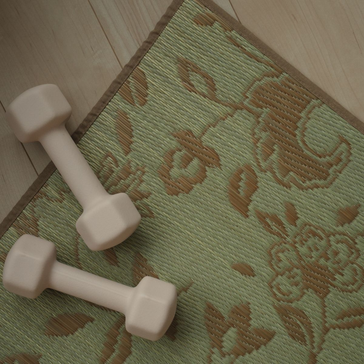 An overhead view of a Japanese Tatami Yoga Mattress "Sarasa" Beige on a wooden floor with a small dumbbell, highlighting the botanical pattern.