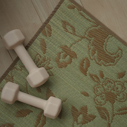 An overhead view of a Japanese Tatami Yoga Mattress "Sarasa" Beige on a wooden floor with a small dumbbell, highlighting the botanical pattern.