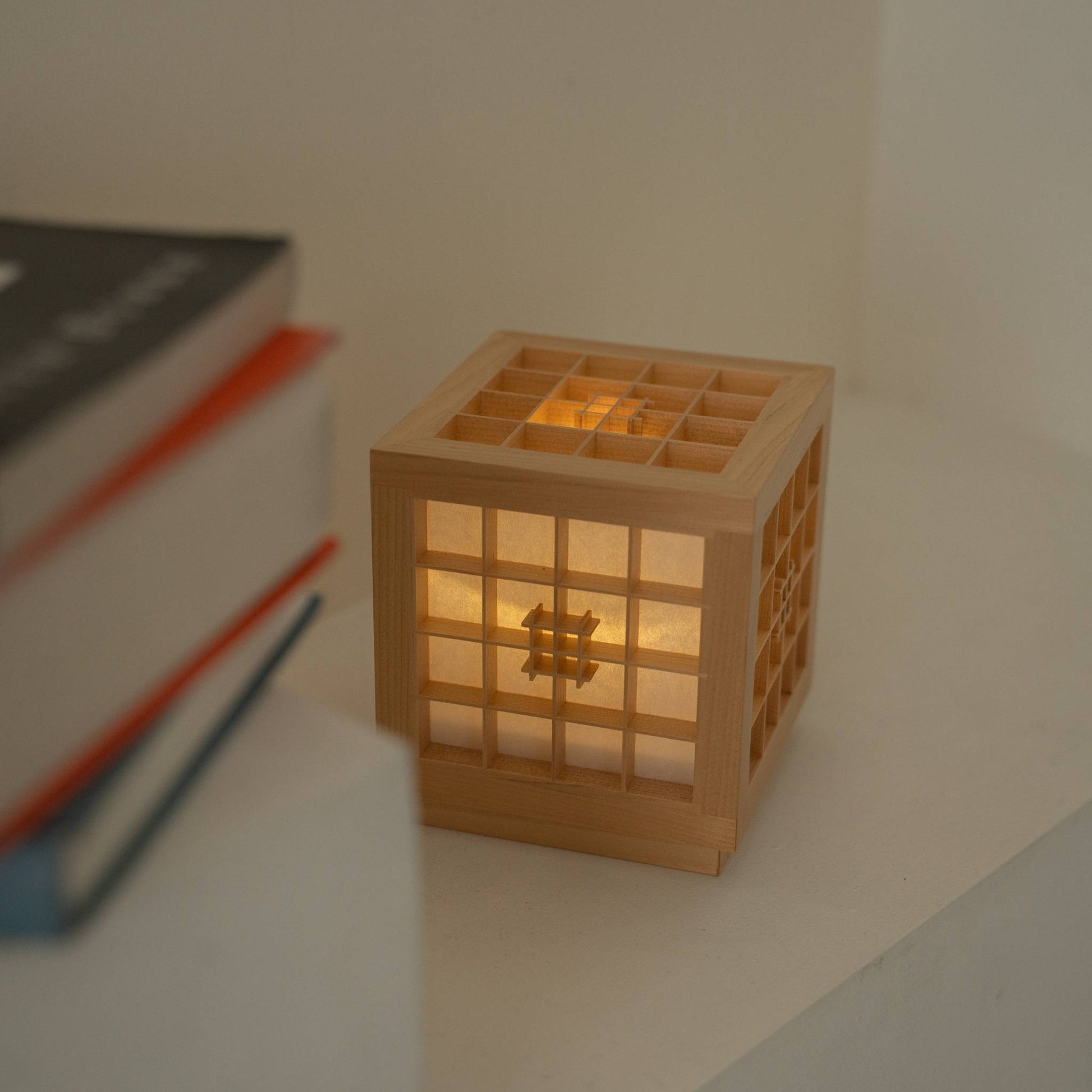 Lit Japanese Wood Table Lamp "Honoka" emitting a warm glow next to books, serving as a cozy cordless accent lamp.