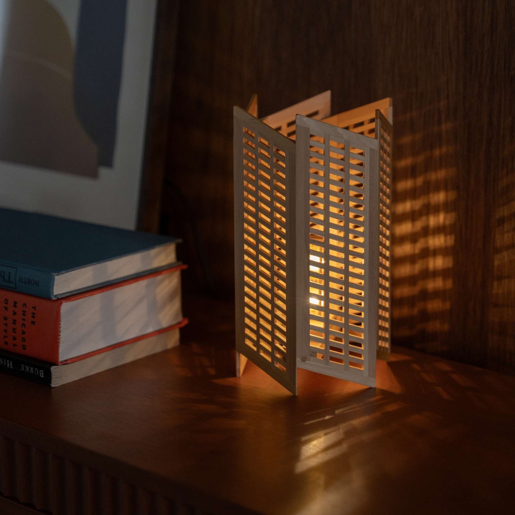 "Lit Japanese wood table lamp \"Towaru\" on a mid-century modern console table, casting striking linear shadows as an ambient lamp."