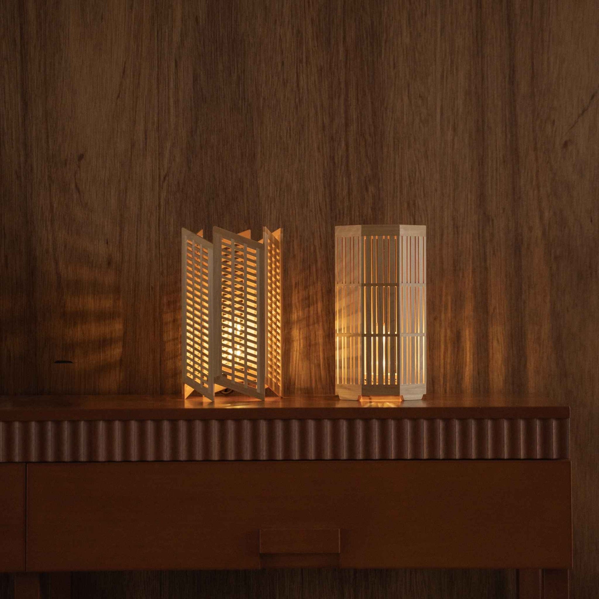 "Lit Japanese wood table lamp \"Towaru\" und \"Kagayaki\", die warme Schatten als Ambientebeleuchtung auf einer Mid-Century-Modern-Konsole werfen."