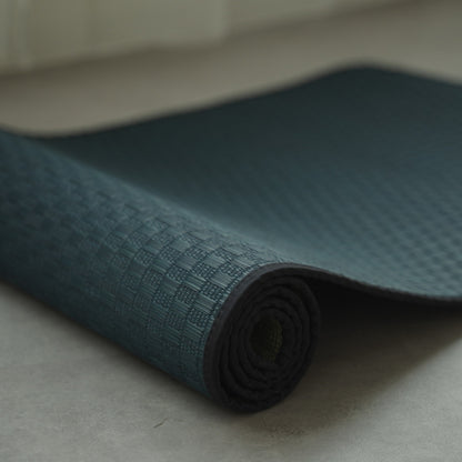 Japanse Tatami Yogamat "Ed Plain" Navy gedeeltelijk opgerold op een grijze vloer, met nadruk op de effen geweven tatami mat textuur.