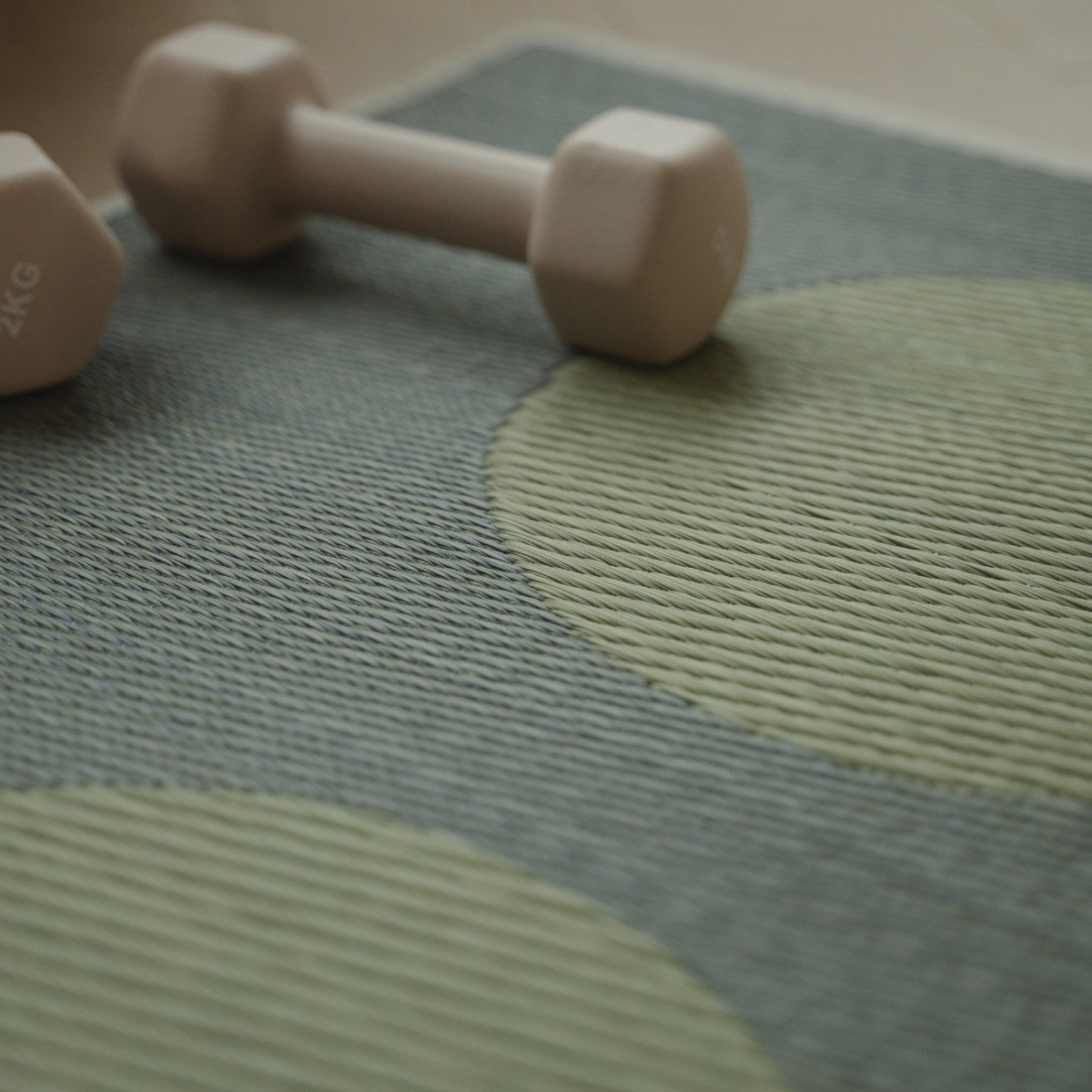 Gedetailleerd beeld van de Japanse Tatami Yoga Mat "Maan" Grijs, met focus op het natuurlijke vlechtpatroon van zeegras en een kleine halter erop.