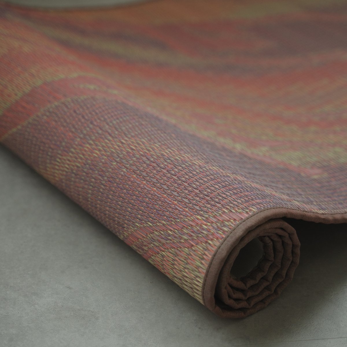 Japanese Tatami Yoga Mattress "Marble" Pink partially rolled on a grey floor, showing the natural woven tatami mat texture.