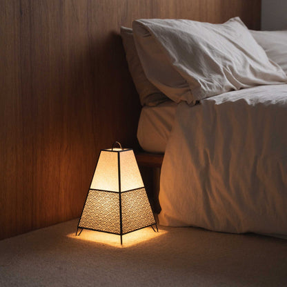 "Lit Japanse vloerlamp KURA Small werpt ingewikkelde schaduwen van zijn papieren kap als sfeerverlichting in een Japandi slaapkamer."