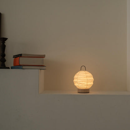 Lit round Japanese paper table lamp "Yuhi" casting a soft glow as an ambient lamp on a white Japandi style console.