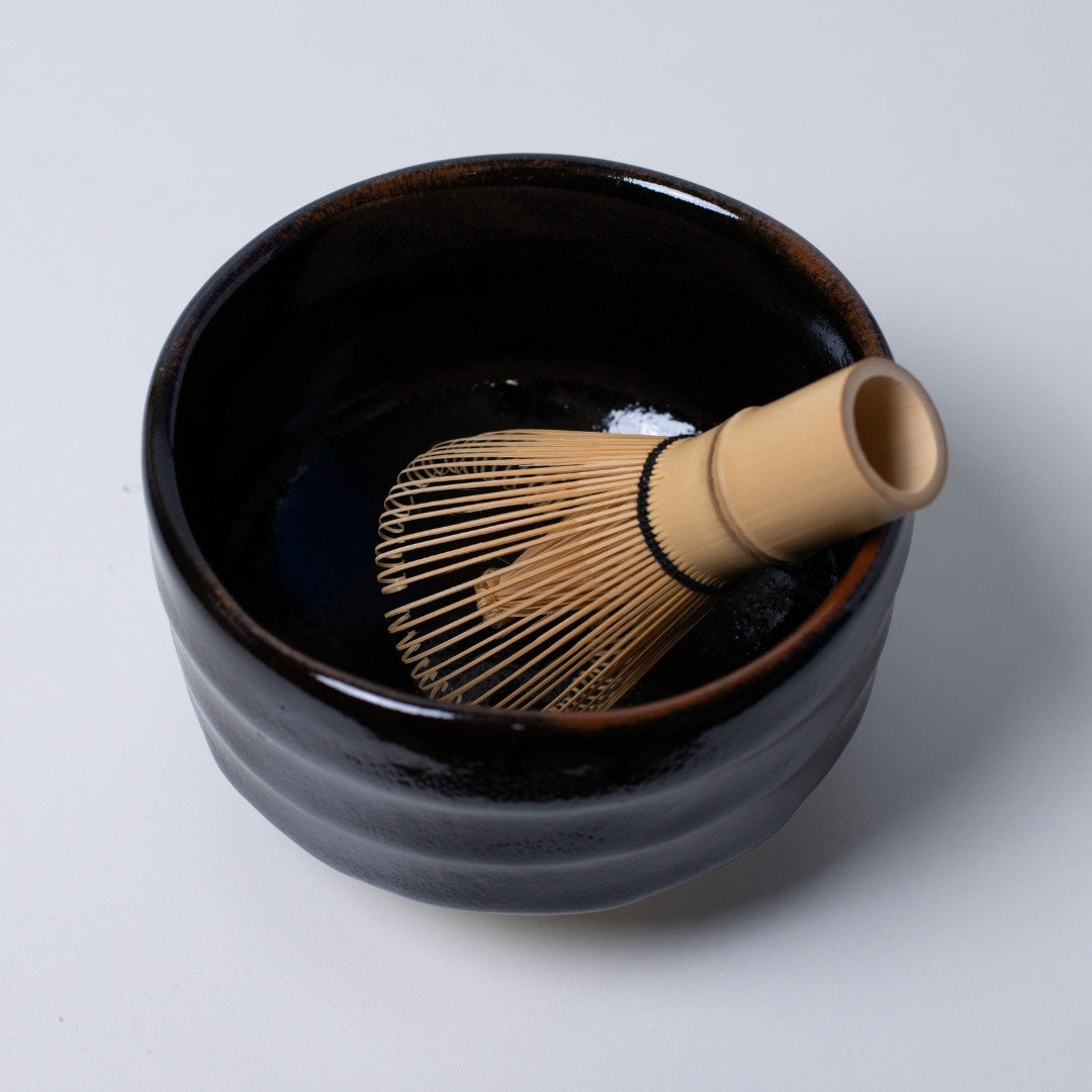 opvisning af "Yuzu Black" japansk matcha-skål med en bambuspisk, der tilbyder en dramatisk kontrast til grønne matcha-te ritualer.