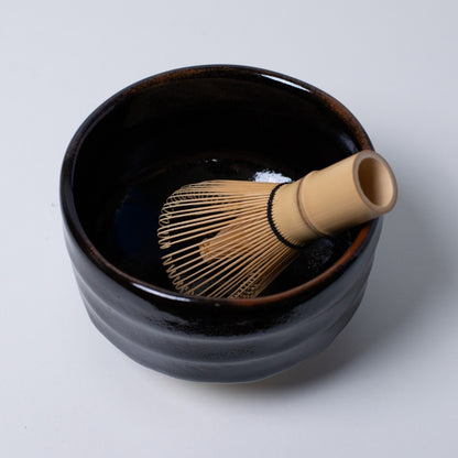 opvisning af "Yuzu Black" japansk matcha-skål med en bambuspisk, der tilbyder en dramatisk kontrast til grønne matcha-te ritualer.