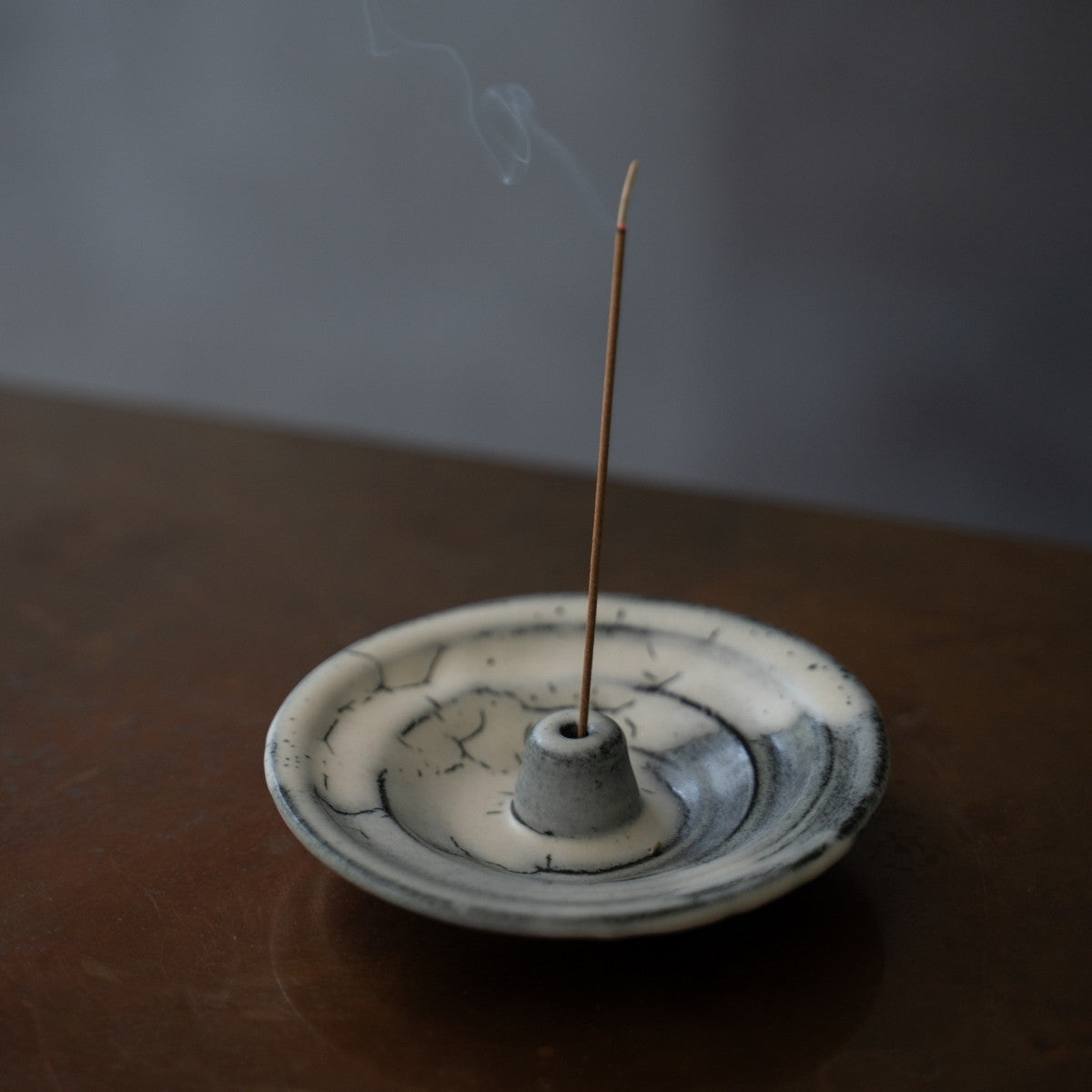 Handcrafted white and black Japanese incense holder with a smoking stick on a dark wood table, setting a tranquil mood for the evening.