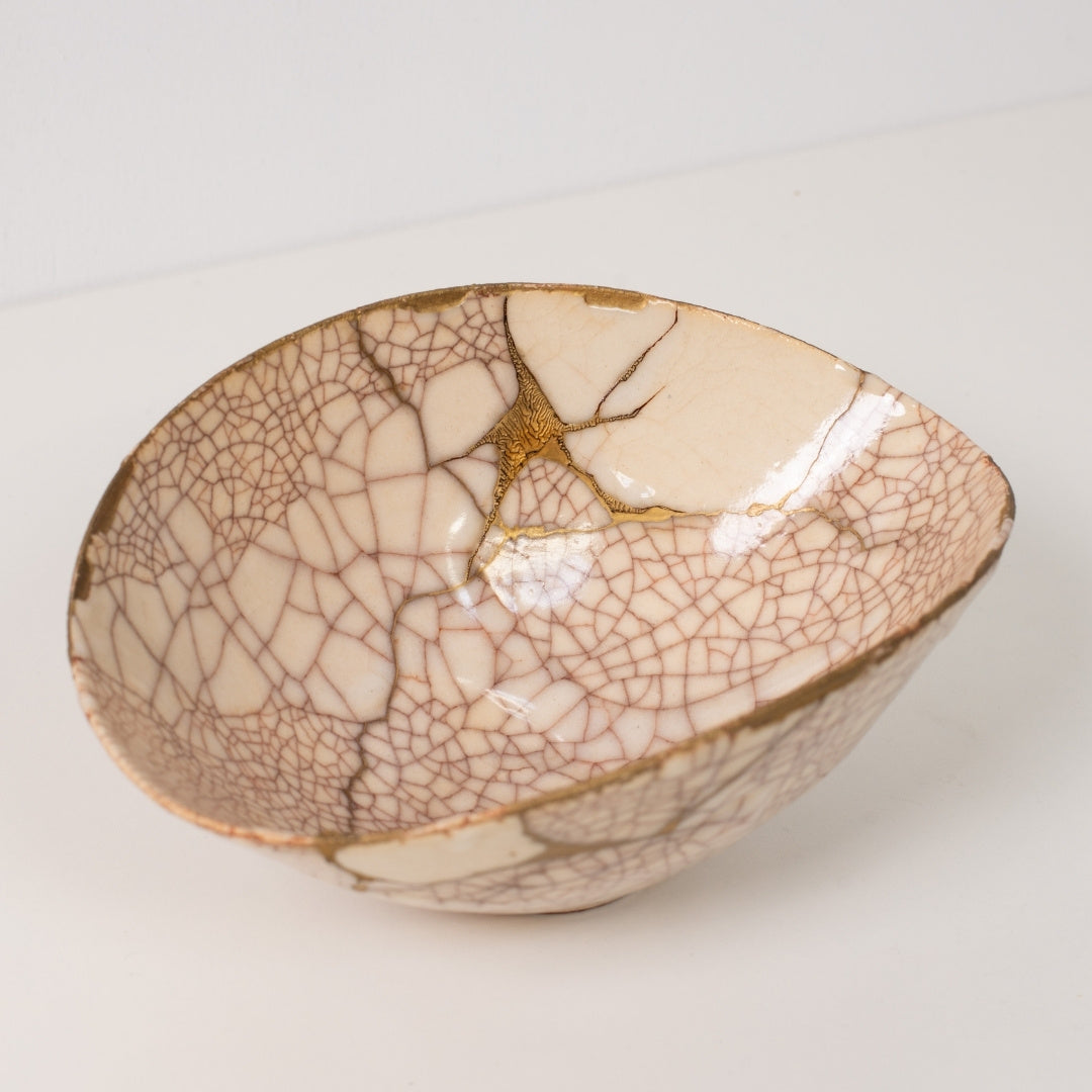 Vue en plongée à l'intérieur d'un bol kintsugi blanc révélant les réparations dorées qui définissent la résilience wabi sabi
