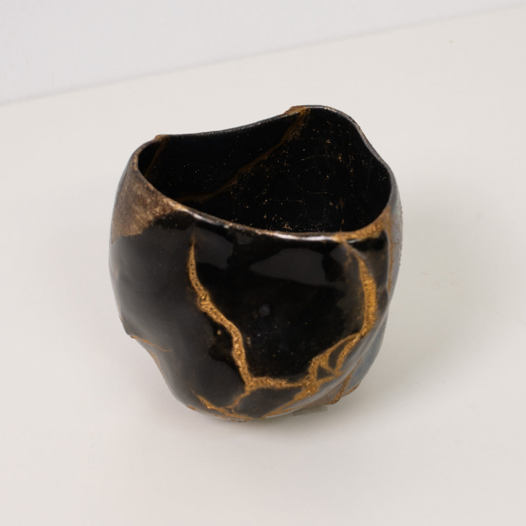 Hohe Ansicht in eine schwarze Kintsugi-Matcha-Schale, die dicke goldene Reparaturen von Wabi-Sabi-Kunst zeigt