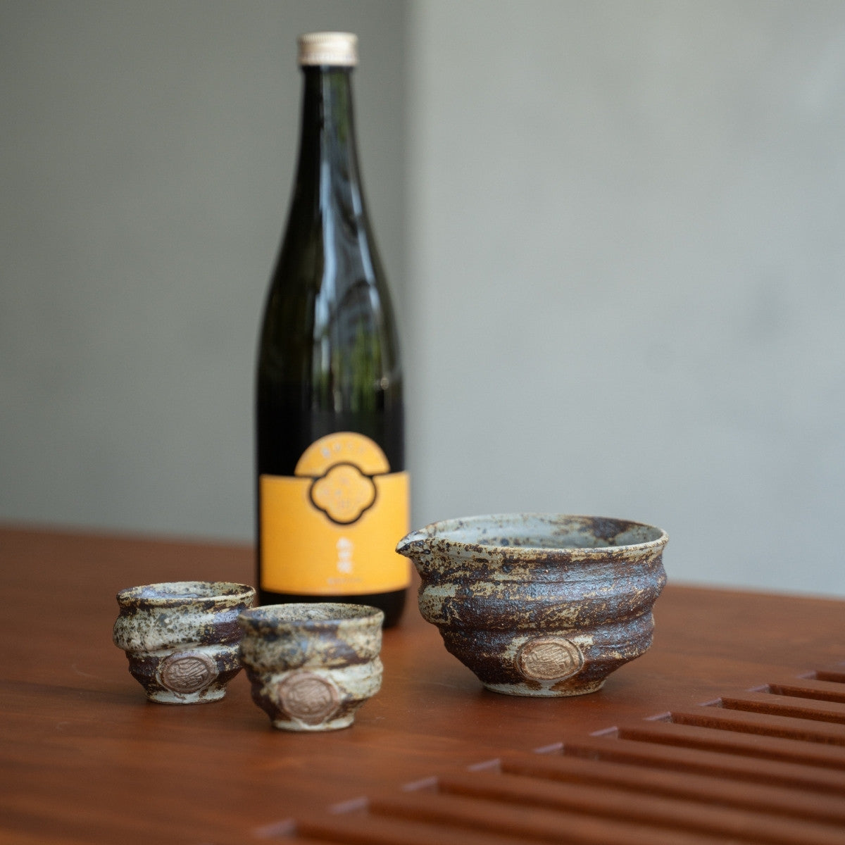 Rustik japansk keramik sake-sæt på et træbord med en flaske, klar til voksne til at nyde en afslappende aften.