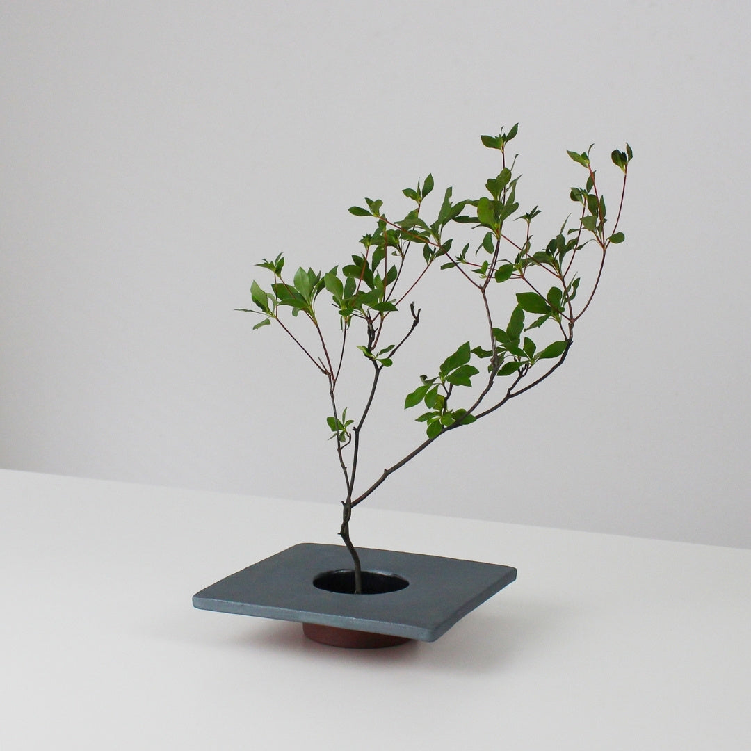 minimalistisk ikebana-vase i jern inspireret af traditionelle japanske tagsten, med en kenzan (blomsterholder) til at arrangere blomster.