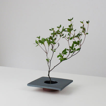 minimalistisk ikebana-vase i jern inspireret af traditionelle japanske tagsten, med en kenzan (blomsterholder) til at arrangere blomster.