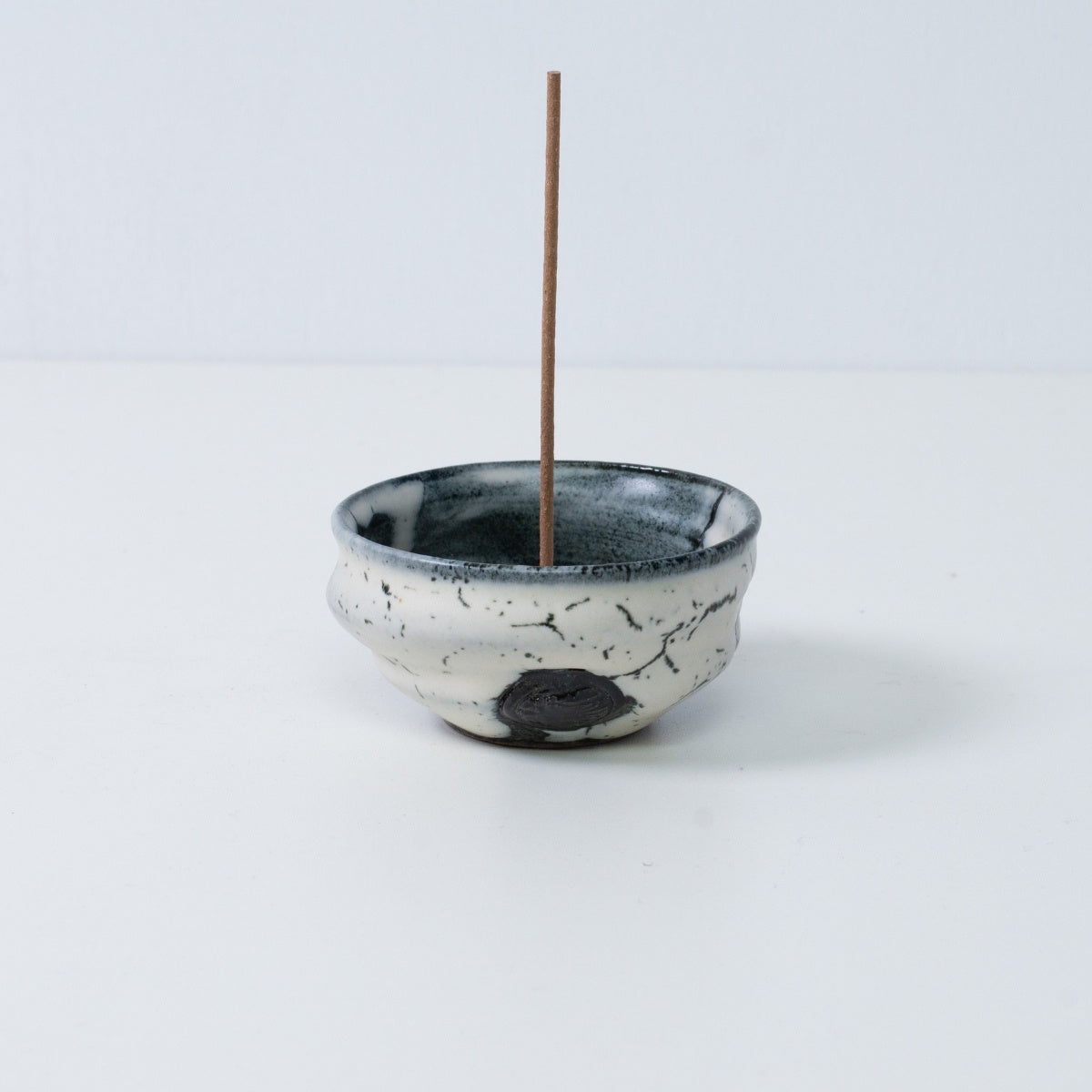 Standalone Japanese incense holder "Creative Cloud" pottery bowl with a stick, showing white and black gradient glaze.