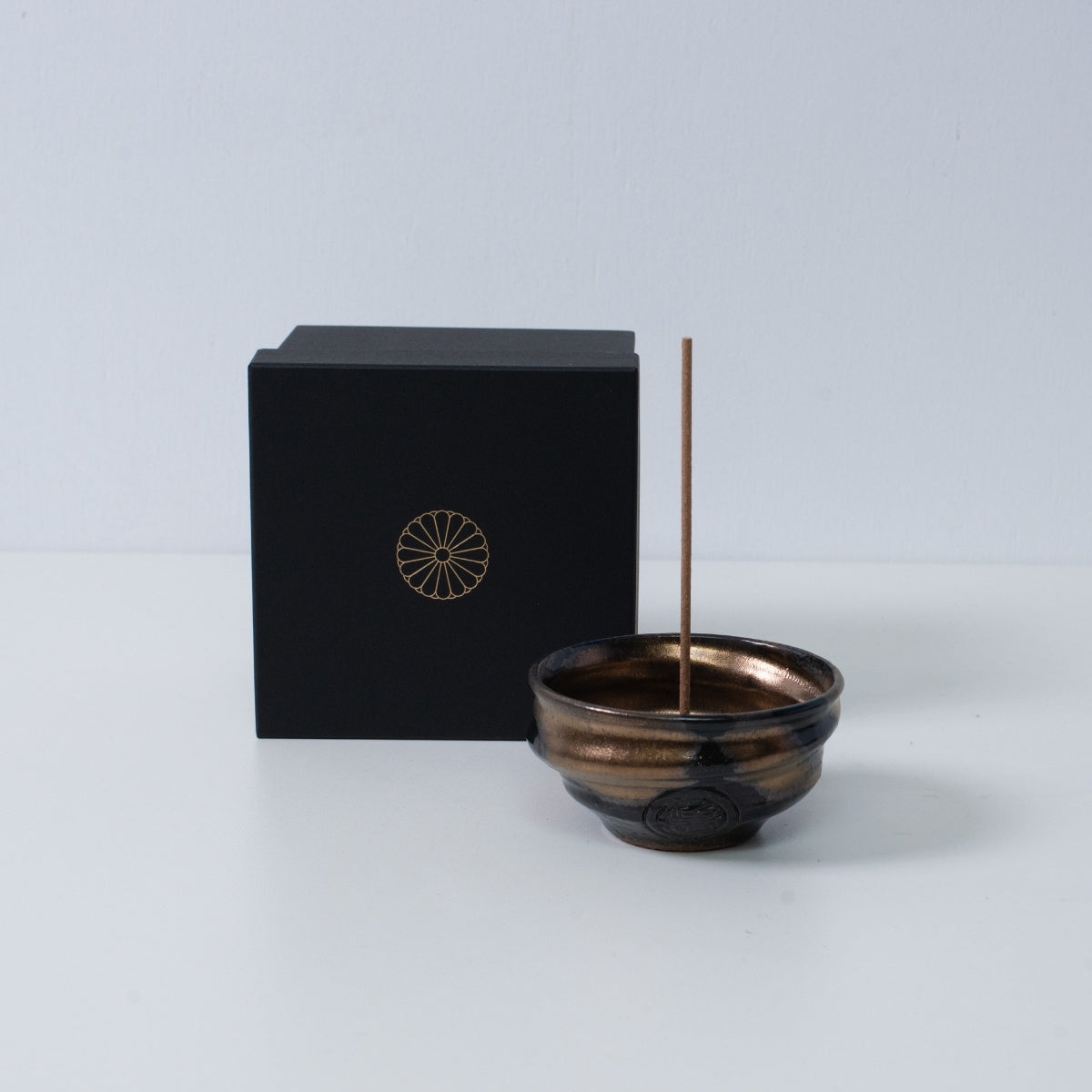 Gouden en zwarte Japanse wierookhouder "Zen" aardewerk schaal met een stokje naast een zwarte geschenkdoos met een gouden chrysant-embleem, Japan.