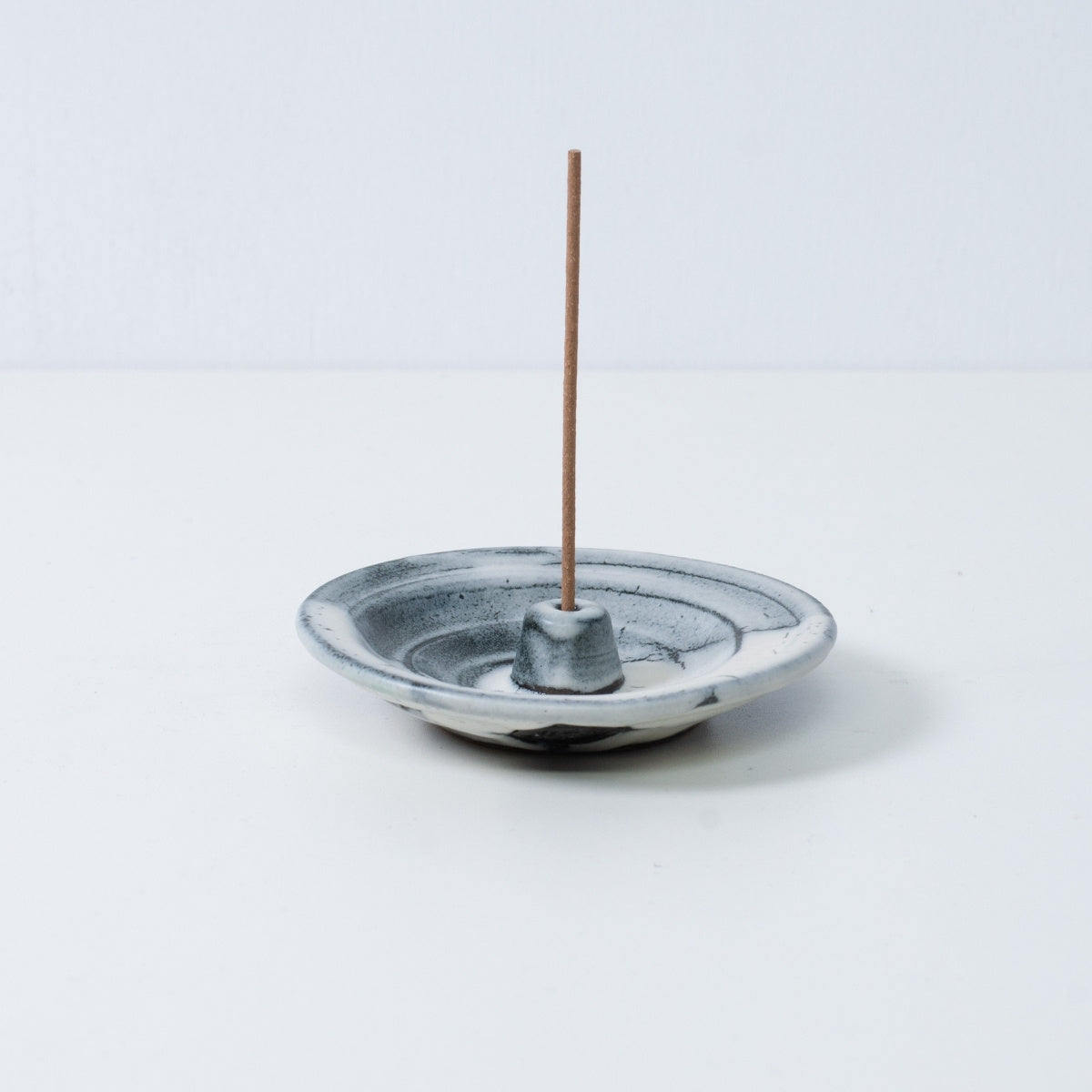 Japanese incense holder "Creative Cloud" pottery tray holding a single stick, showing the white and black gradient glaze.
