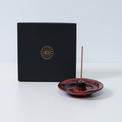 Crimson og sort japansk røgelsesholder "Nobel Red" keramik med en pind ved siden af en sort gaveæske med et gyldent krysantemum-emblem, lavet i Japan.
