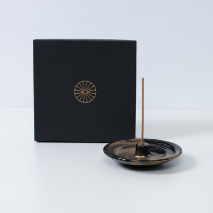 Goldfarbener und schwarzer japanischer Räucherstäbchenhalter "Zen" aus Keramik mit einem Stäbchen neben einer schwarzen Geschenkbox mit goldenem Chrysanthemenwappen, hergestellt in Japan.