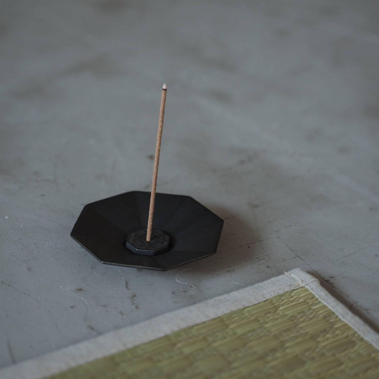 Sort ottekantet japansk røgelsesskål lavet af arita-porcelæn med en brændende pind nær en tatami-måtte.