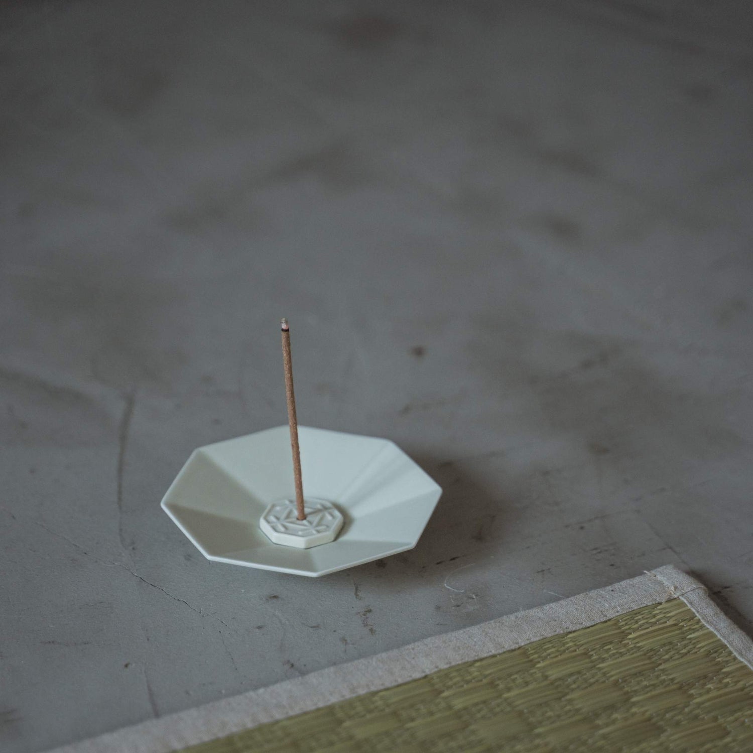 Witte achthoekige porseleinen Japanse wierookbrander met een brandende stok in een minimalistische zenmeditatieruimte.