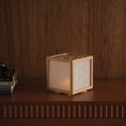 Glimrende japansk kumiko lampeskærm, der sidder på en mørk træhylde ved siden af bøger og skaber en varm og elegant atmosfære.