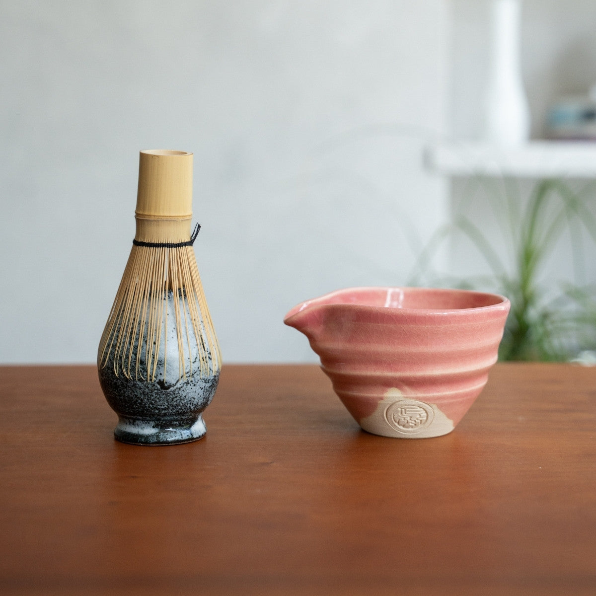 Pink matcha bowl with spout and Japanese matcha whisk stand on a wooden table, preparing for a calming morning tea ritual.