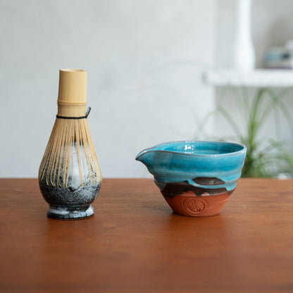 Japanese matcha whisk stand and emerald matcha bowl with spout on a wood table, ready for a calming morning tea ritual.