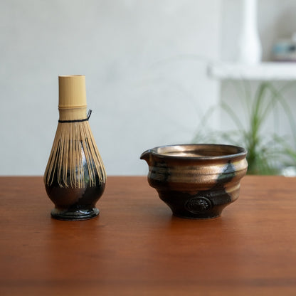 Support de fouet à matcha japonais et bol à matcha avec bec verseur sur une table en bois, gardant les outils prêts pour une routine de bien-être quotidienne.