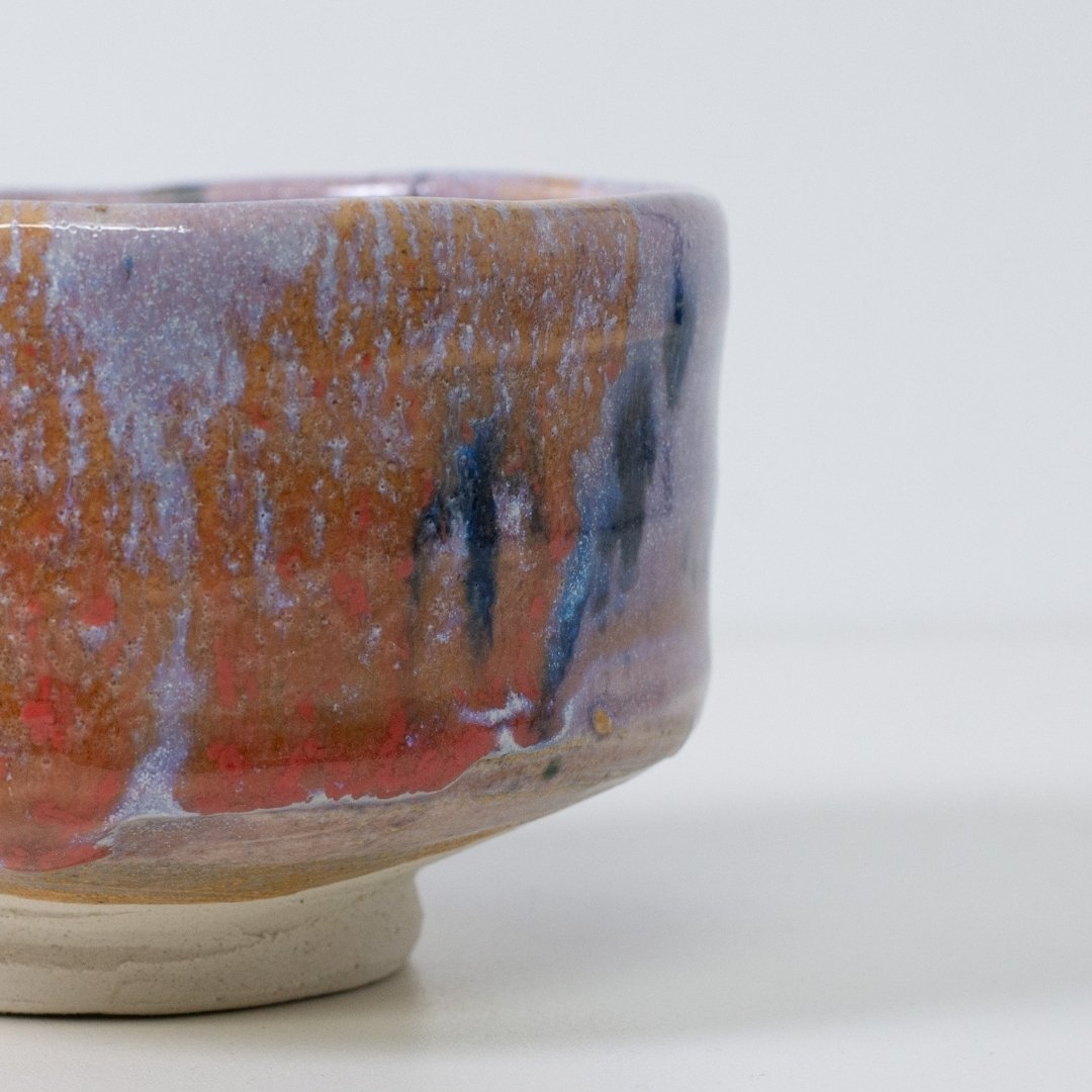 Tæt på detalje af "Navy & Red Splash" matcha-skål, der viser den kunstneriske Kinyo-glasurtekstur med røde og marineblå dryp over en lyslilla bund.