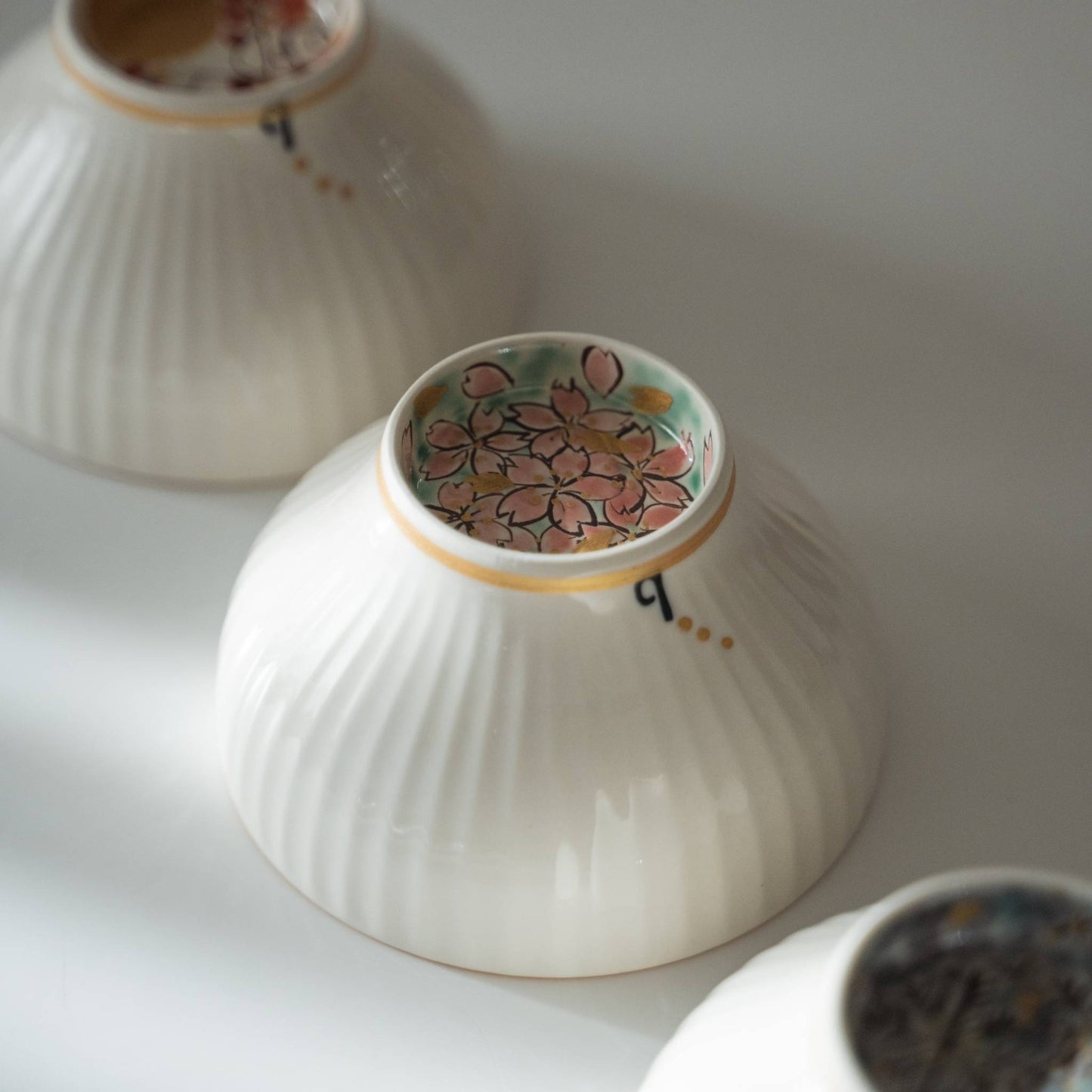 Bund af en japansk matcha-skål med et skjult sakura-blomstermotiv, håndmalet i guld og pink.