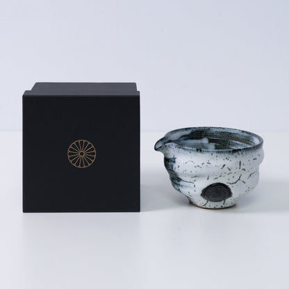 White and black Japanese matcha bowl with spout "Creative Cloud "pottery beside a black gift box with a gold chrysanthemum crest, from Japan.