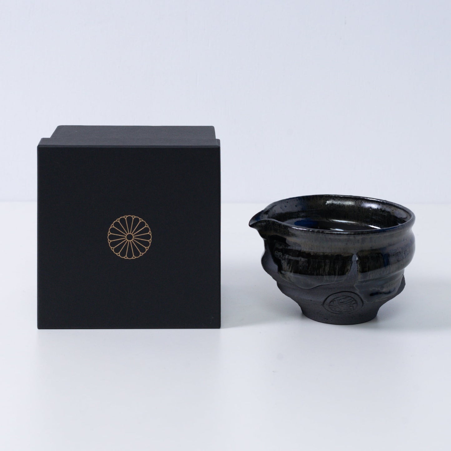 Japanese matcha bowl with spout "Dignity Blue" pottery beside a black gift box with a gold chrysanthemum crest, from Japan.