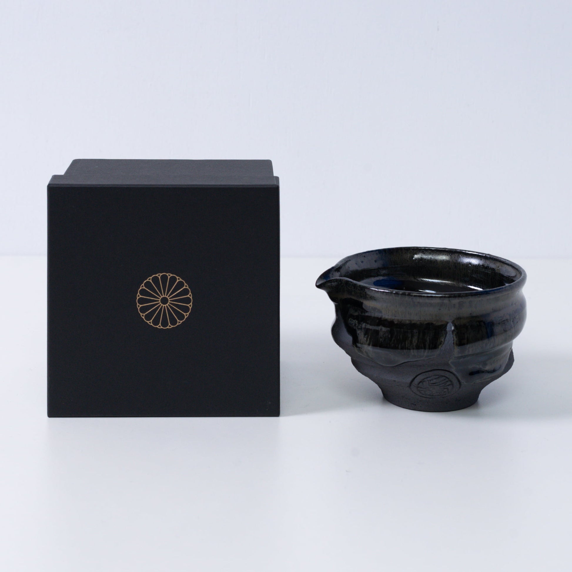 Japanese matcha bowl with spout "Dignity Blue" pottery beside a black gift box with a gold chrysanthemum crest, from Japan.