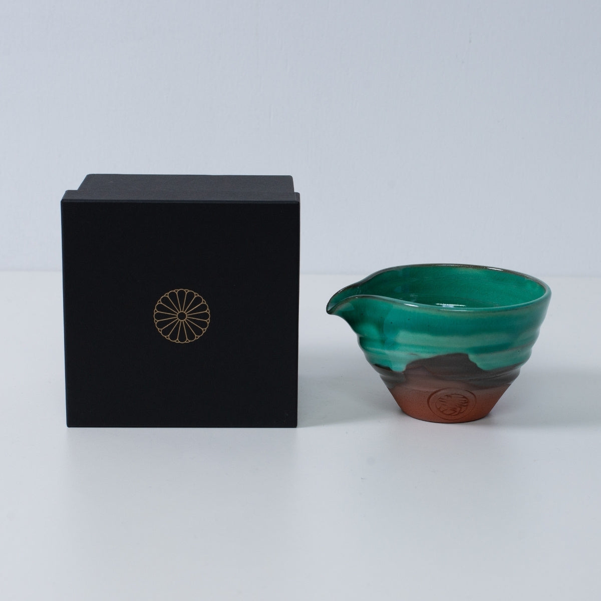 Japansk matcha-skål med tud "Smaragd" keramik ved siden af en sort gaveæske med et gyldent krysantemum-emblem, lavet i Japan.