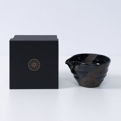 Japanese matcha bowl with spout "Sumi Black" pottery next to a black gift box with a gold imperial chrysanthemum crest, Kyoto ceramics.