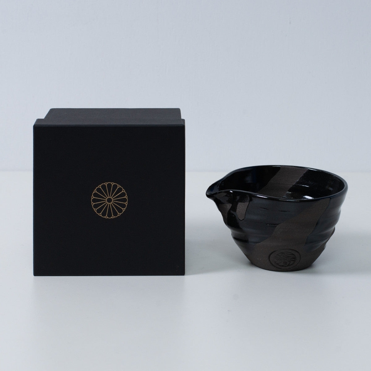 Japansk matcha-skål med tud "Sumi Black" keramik ved siden af en sort gaveæske med et gyldent kejserligt krysantemum-emblem, Kyoto keramik.
