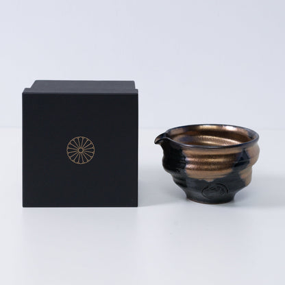 Gold and black Japanese matcha bowl with spout "Zen" pottery next to a black gift box with a gold chrysanthemum crest, made in Japan.