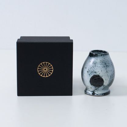 White and black Japanese matcha whisk stand "Creative Cloud" pottery next to a black gift box with a gold chrysanthemum crest, from Japan.