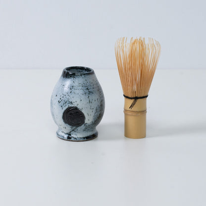 White and black Japanese matcha whisk stand "Creative Cloud" pottery standing next to a traditional bamboo matcha tea whisk, Japan.
