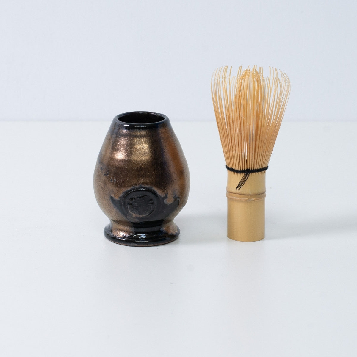 Support en céramique noir et or pour fouet à matcha japonais "Zen", placé à côté d'un fouet traditionnel en bambou pour matcha chasen, Japon.