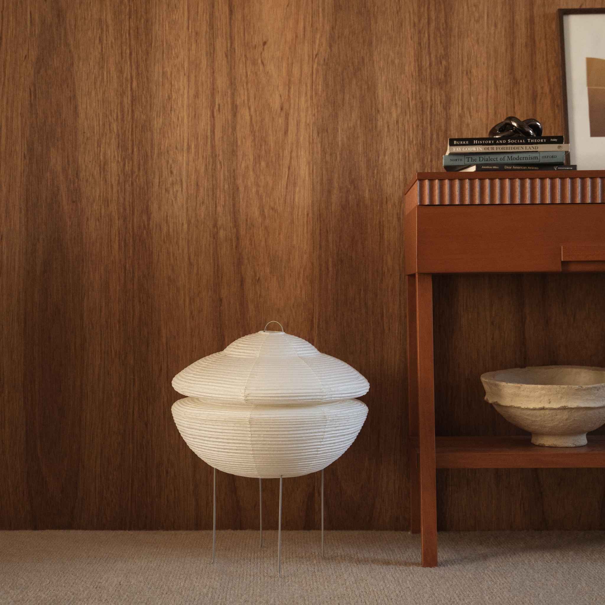 Lampe sur pied japonaise non allumée en papier Gemini 01 posée sur un tapis à côté d'une console en bois devant un mur en bois